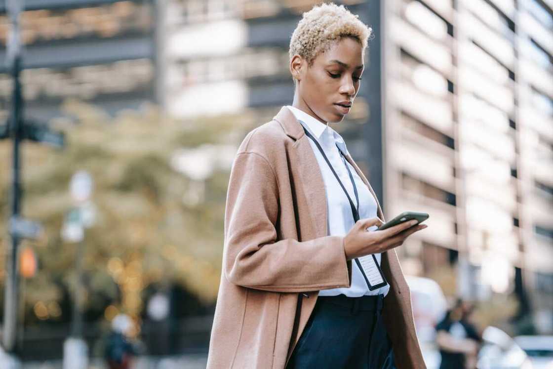 A woman with blonde hair and a brown coat is using a smartphone