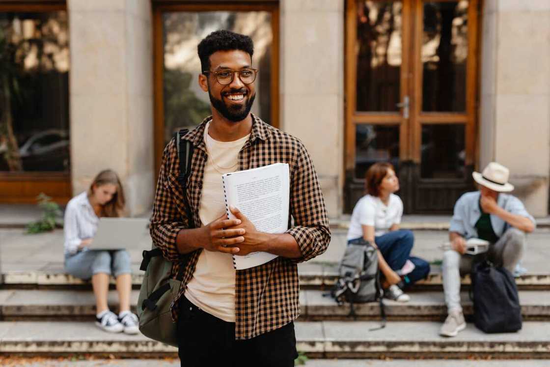 Male student walking out from university, carrying a book