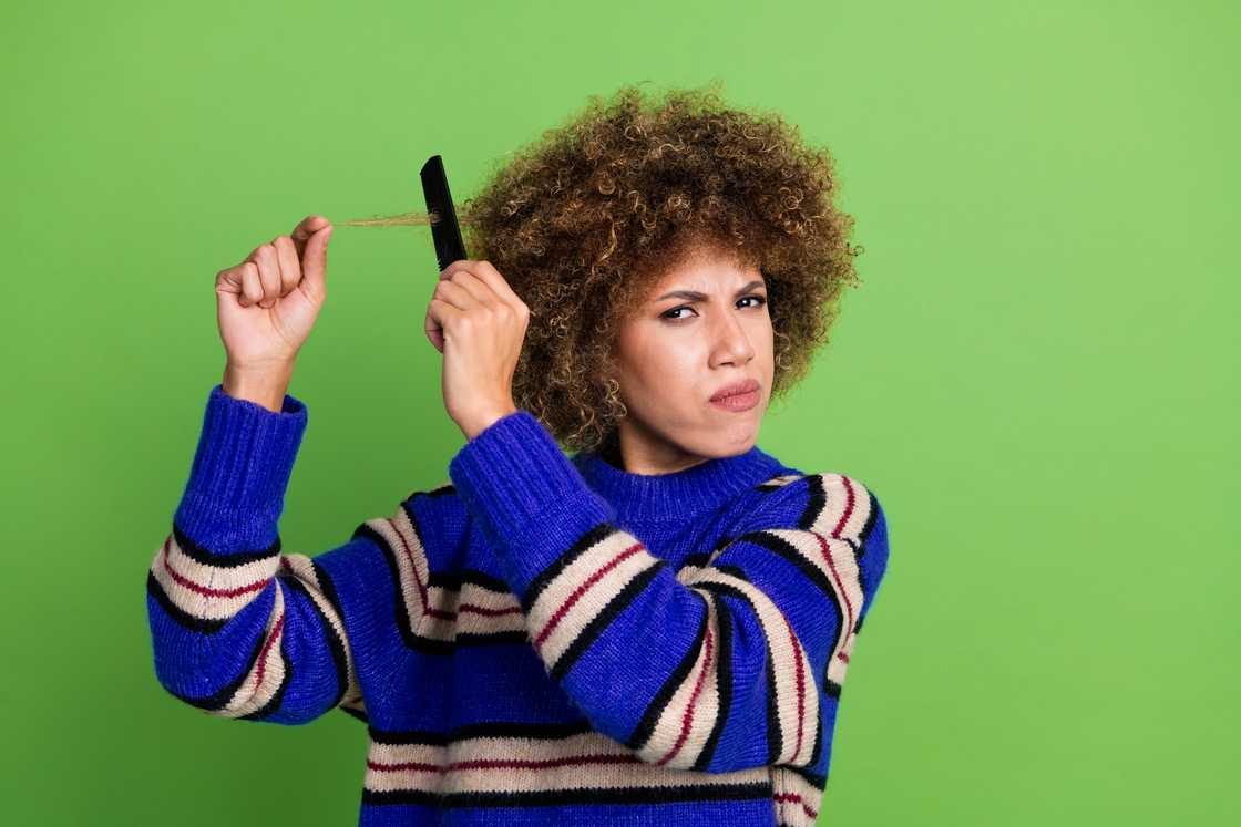 An unhappy woman holding frizz hardly combing hair