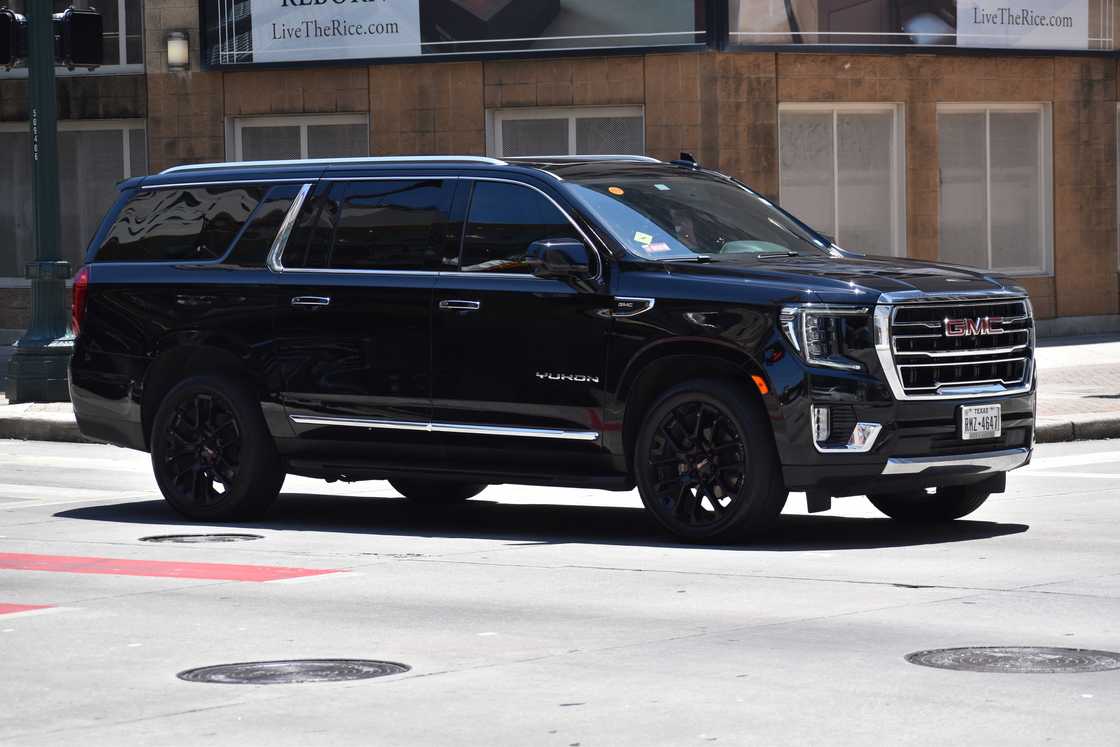 A portrait of a black GMC Yukon XL cruising in a downtown financial district.