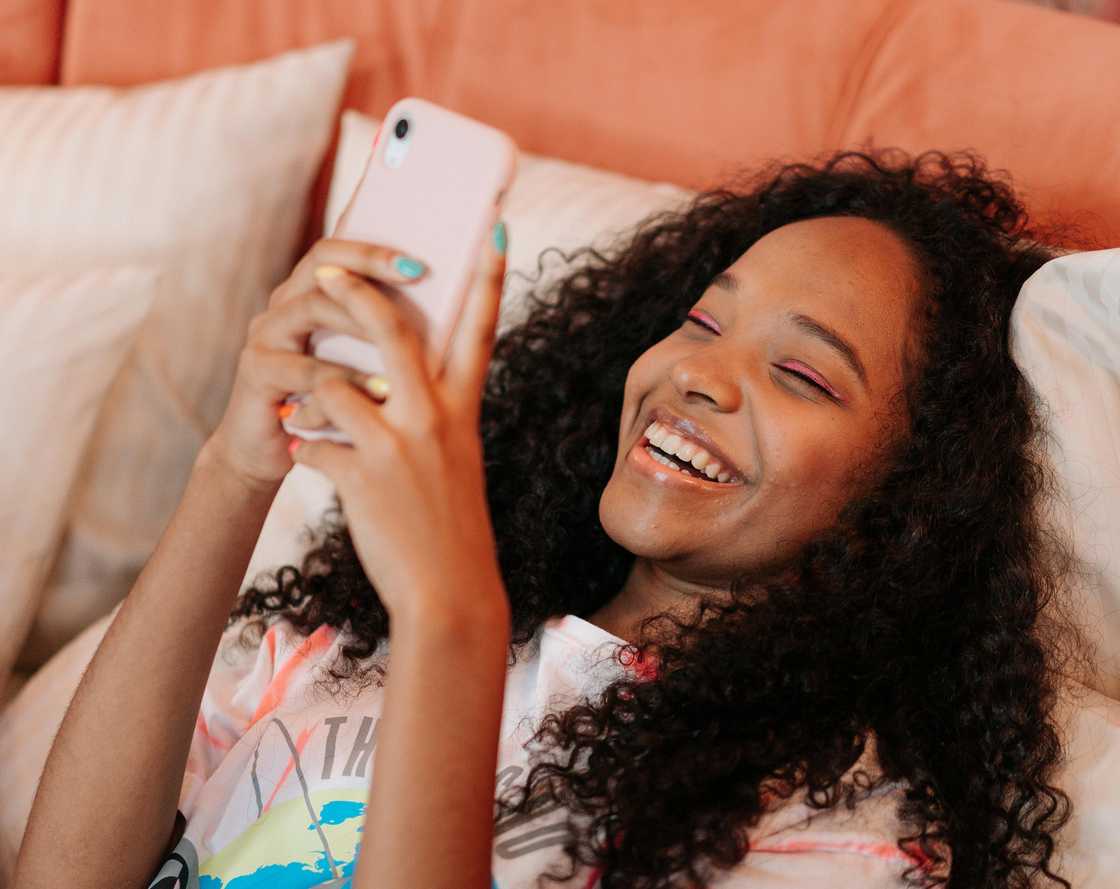 A teenage girl laughing with a smartphone on the bed