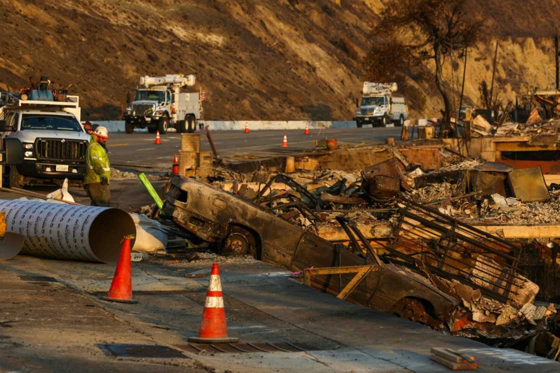 Edison employees look at burned remains of a car as they work to restore electricity along the Pacific Coast Highway in Malibu, California on January 19, 2025