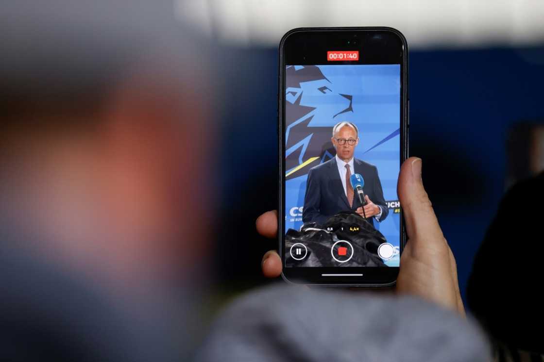 A person holding a mobile phone that shows an address by Friedrich Merz, leader of Germany's Christian Democratic Union